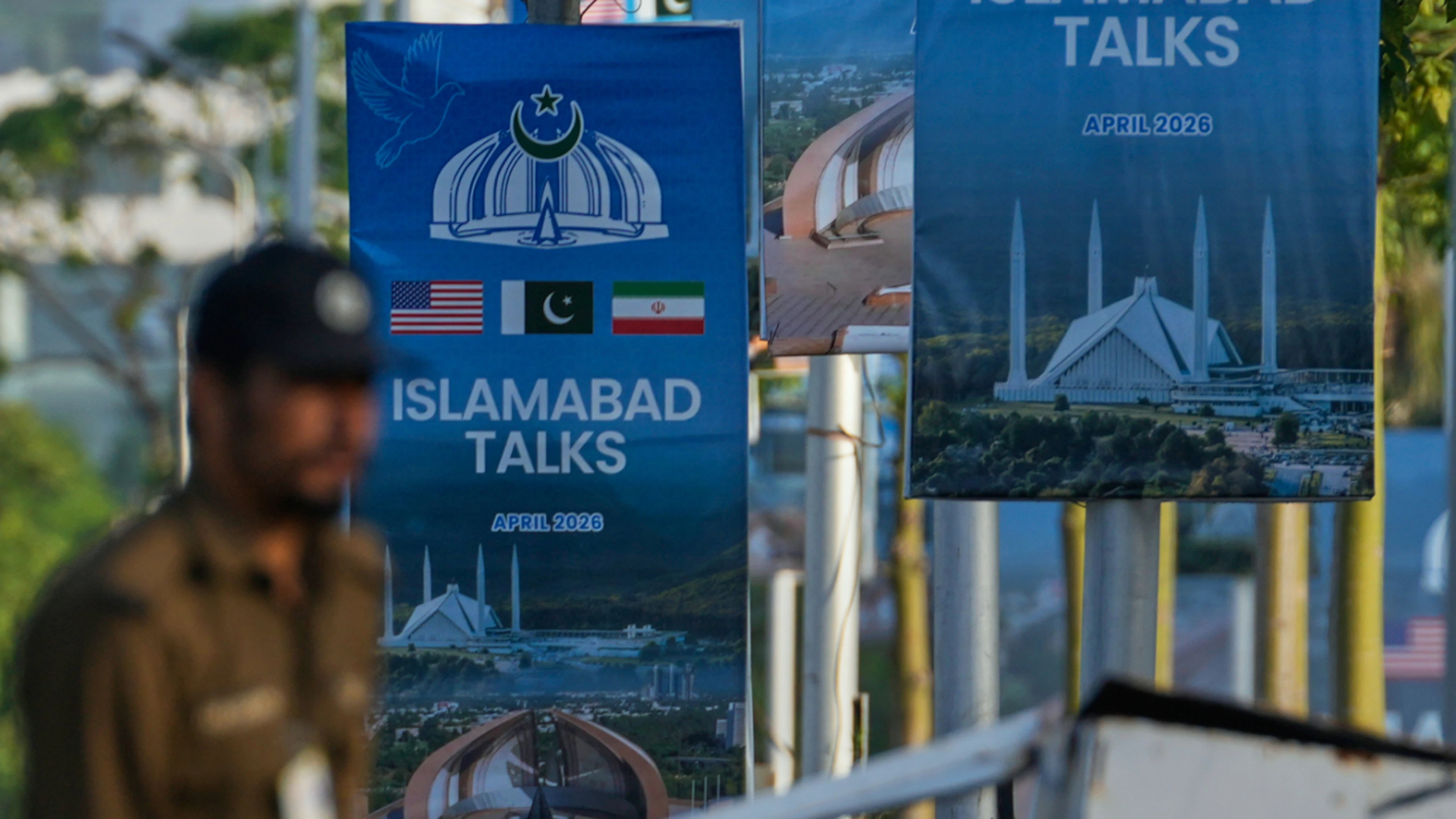 ARCHIV – Ein Polizist geht an Plakaten für die Gespräche zwischen den USA und dem Iran in der Nähe eines möglichen Verhandlungsortes vorbei. Foto: Anjum Naveed/AP/dpa (Archivbild)