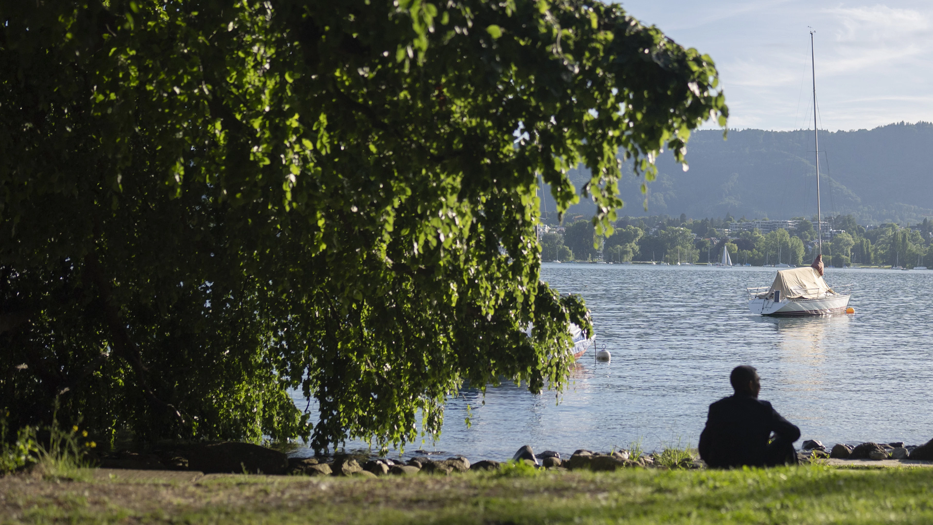 A man is sitting on the shore of Lake Zurich.